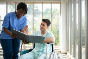 Nurse assisting explains therapy to a disabled patient in a wheelchair at the hospital.